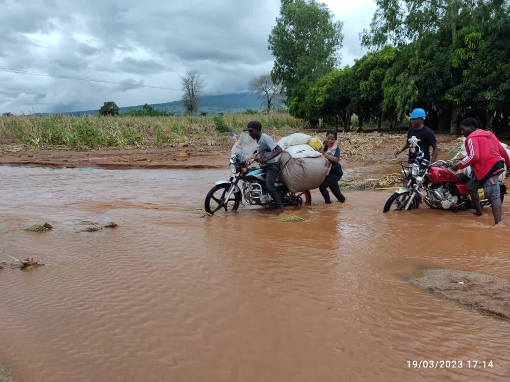 Community members crossing floodwater on motorbikes carrying supplies